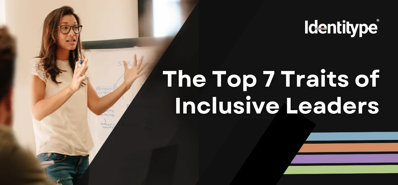 A woman in a casual white top and glasses is gesturing towards a flip chart during a presentation, with text on the right saying 'The Top 7 Traits of Inclusive Leaders' beside the Identitype® logo with a multicolored underline.